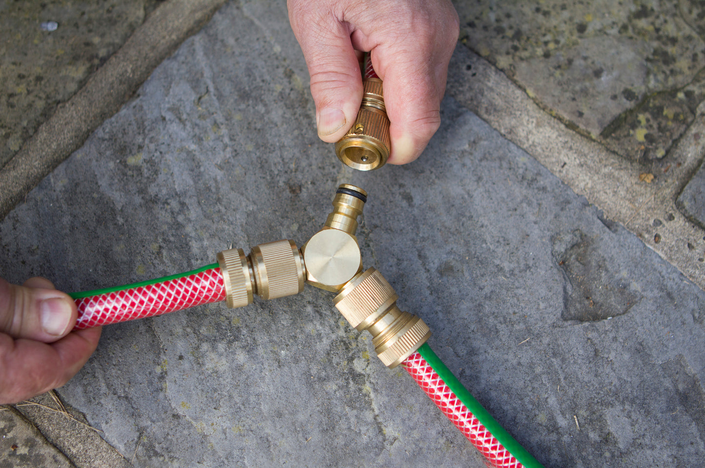 Hand connecting a garden hose to a brass fitting on a stone pavement.