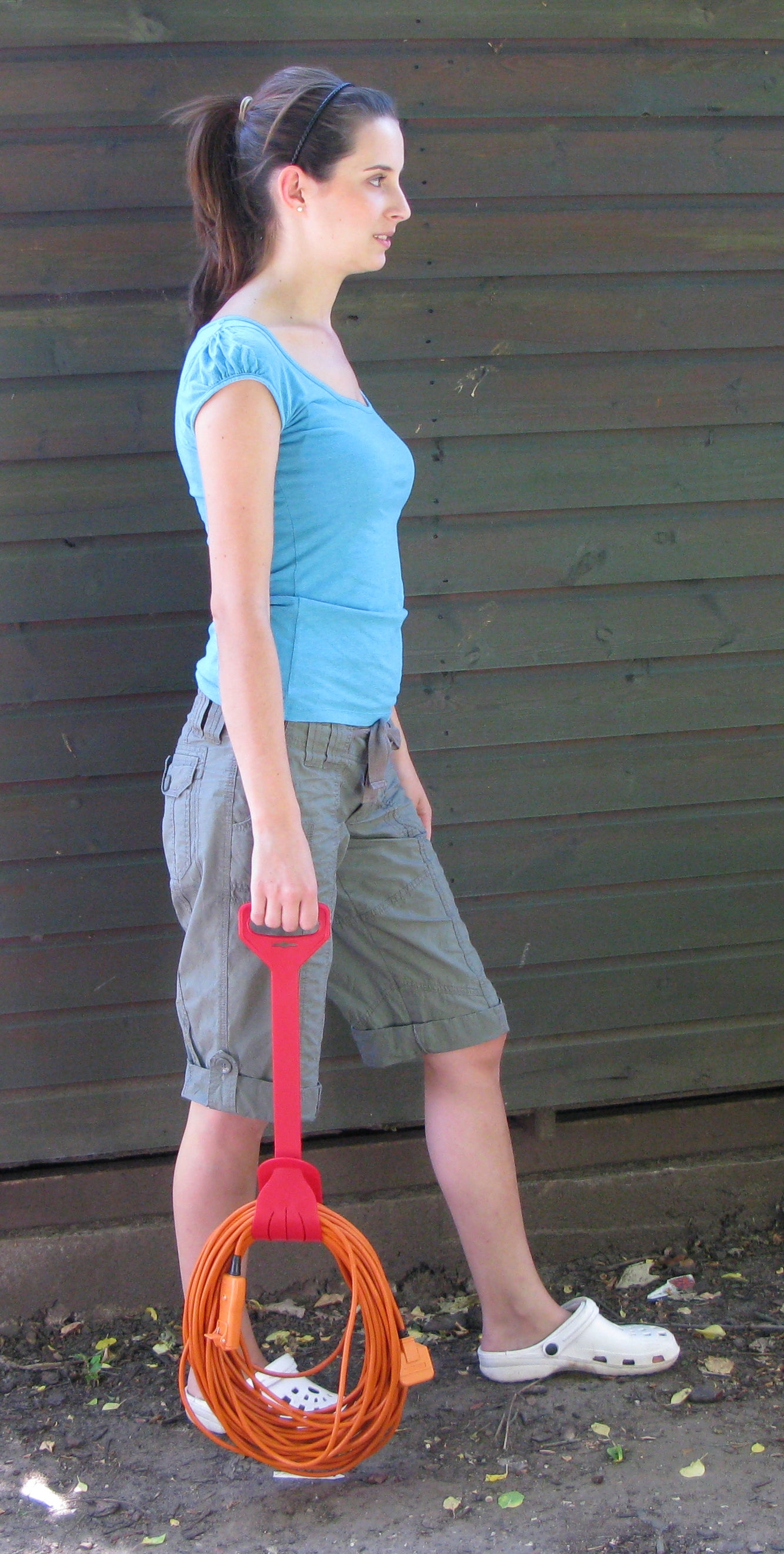 Woman holding an orange extension cord with a red handle against a wooden wall.