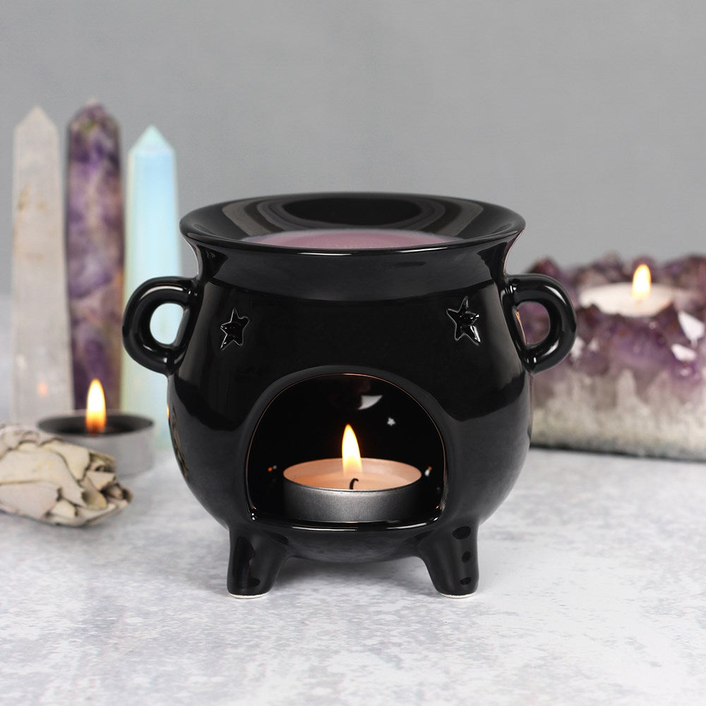 Black ceramic oil burner with a lit candle inside, surrounded by crystals and candles on a gray surface.
