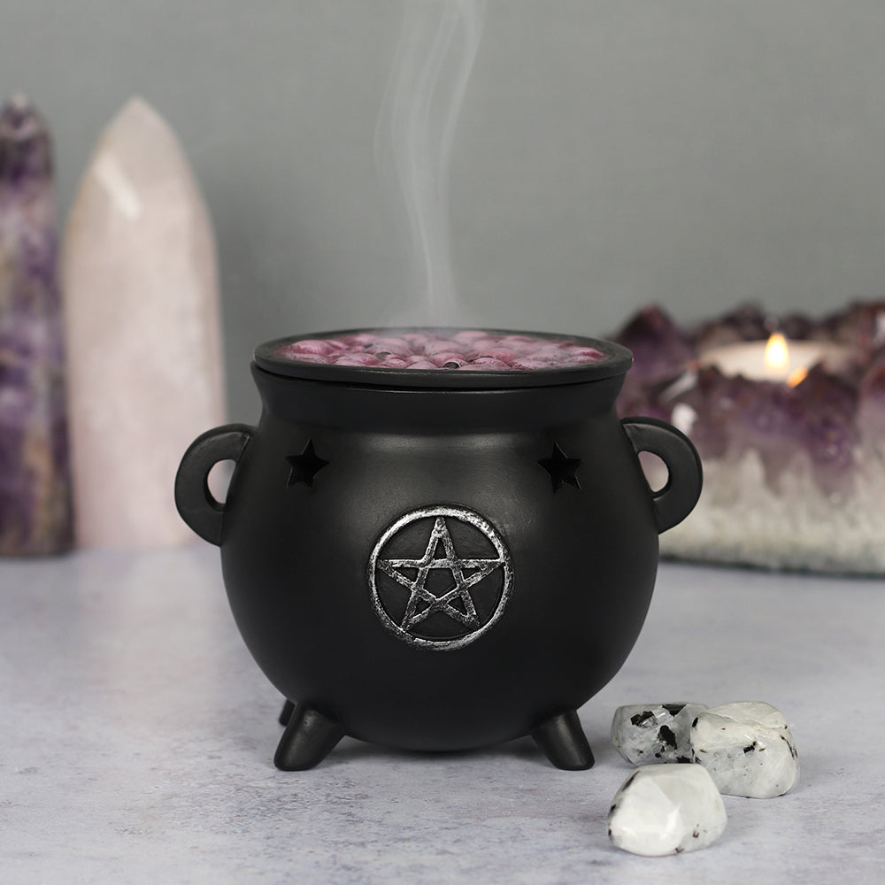 Black cauldron with a pentagram design, incense burning inside, on a neutral background with crystals.