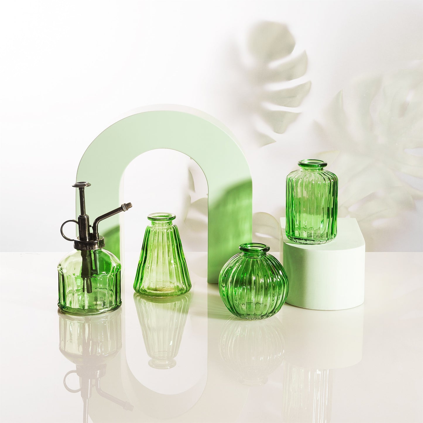 Green glass vases on a white surface with a light green arch in the background