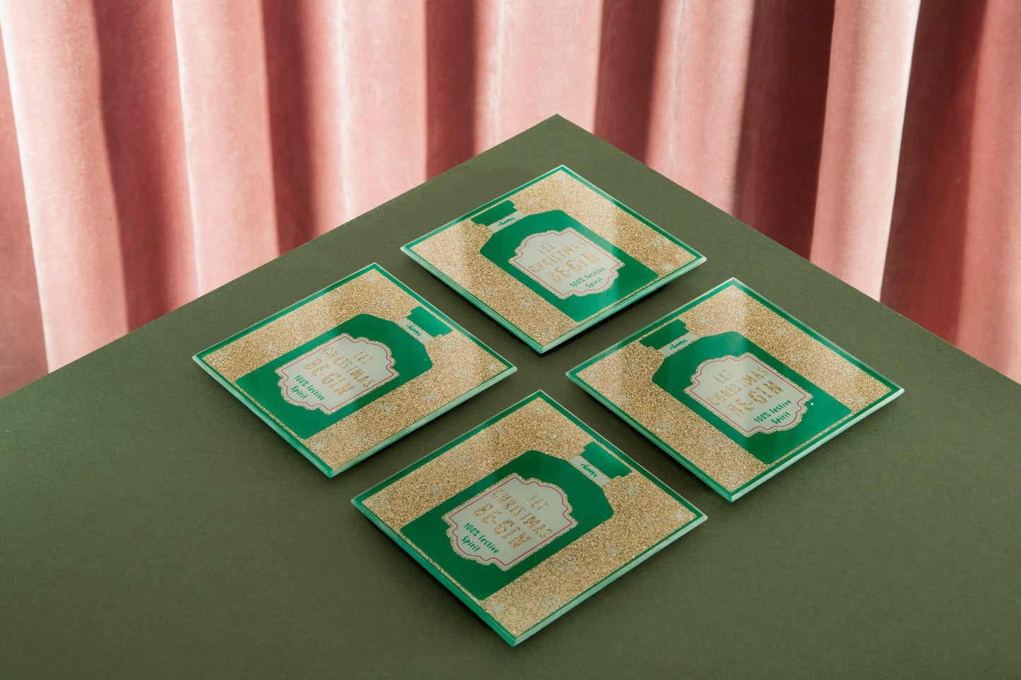 Four green and gold cards on a green surface with pink curtains in the background