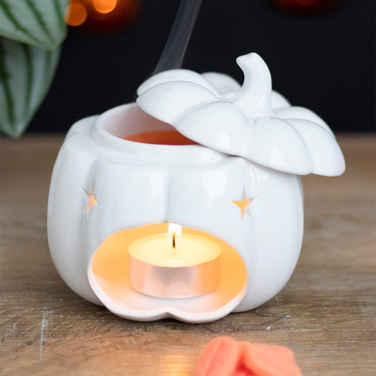 White ceramic pumpkin-shaped candle holder with a lit candle inside on a wooden surface.