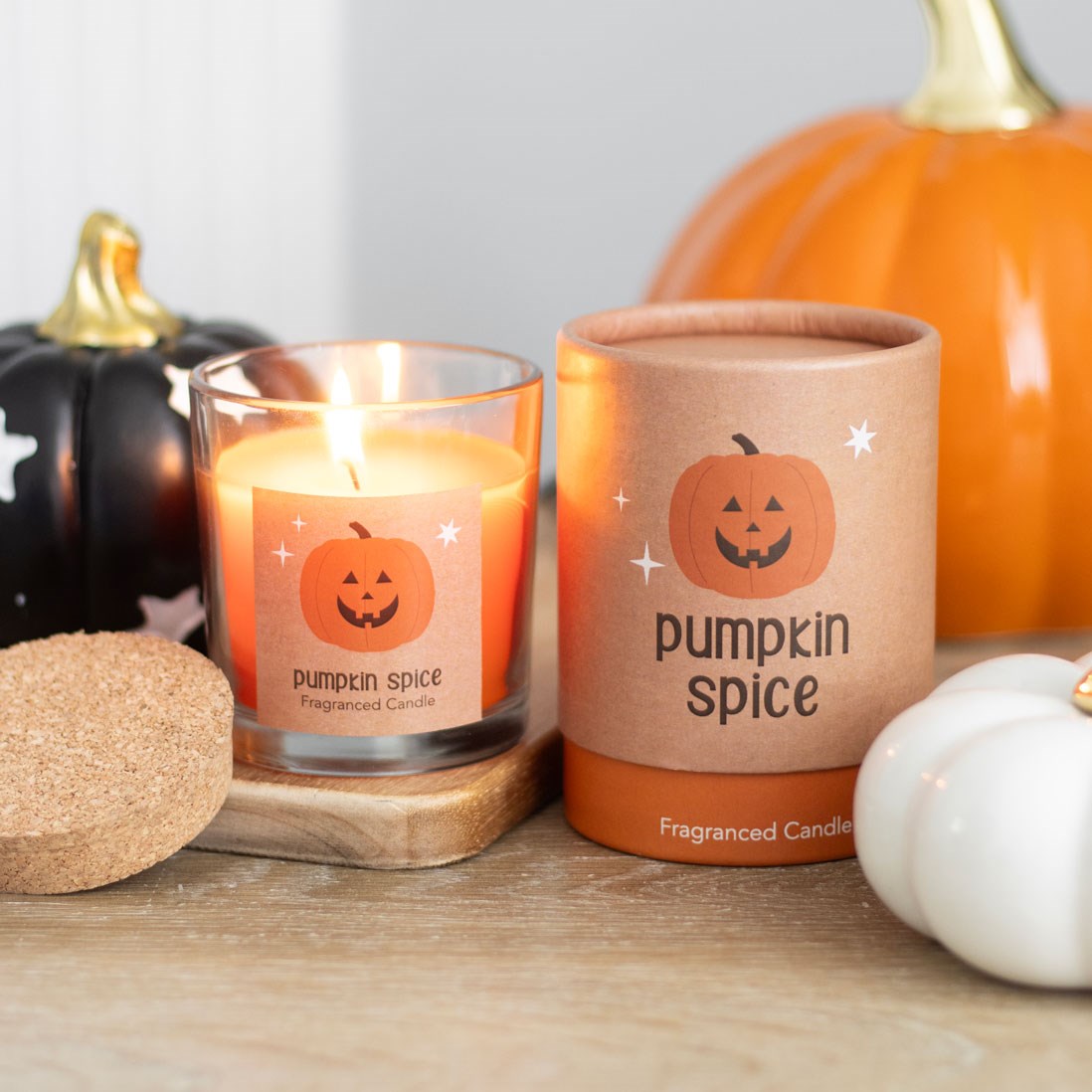 Pumpkin spice candle with packaging and pumpkins on a wooden surface