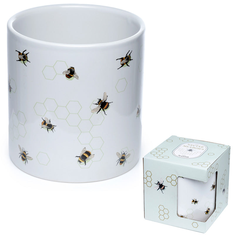 White mug with bee and honeycomb pattern next to a matching candle in a box on a white background