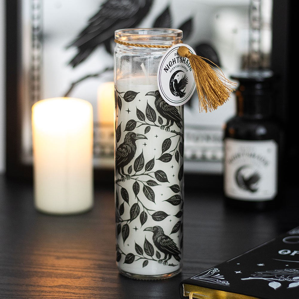 Decorative candle with bird and leaf pattern in a glass jar on a dark surface.
