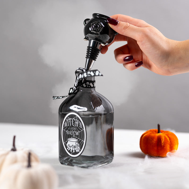 Bottle labeled 'Witch's Brew' with a hand opening it, surrounded by pumpkins on a neutral background