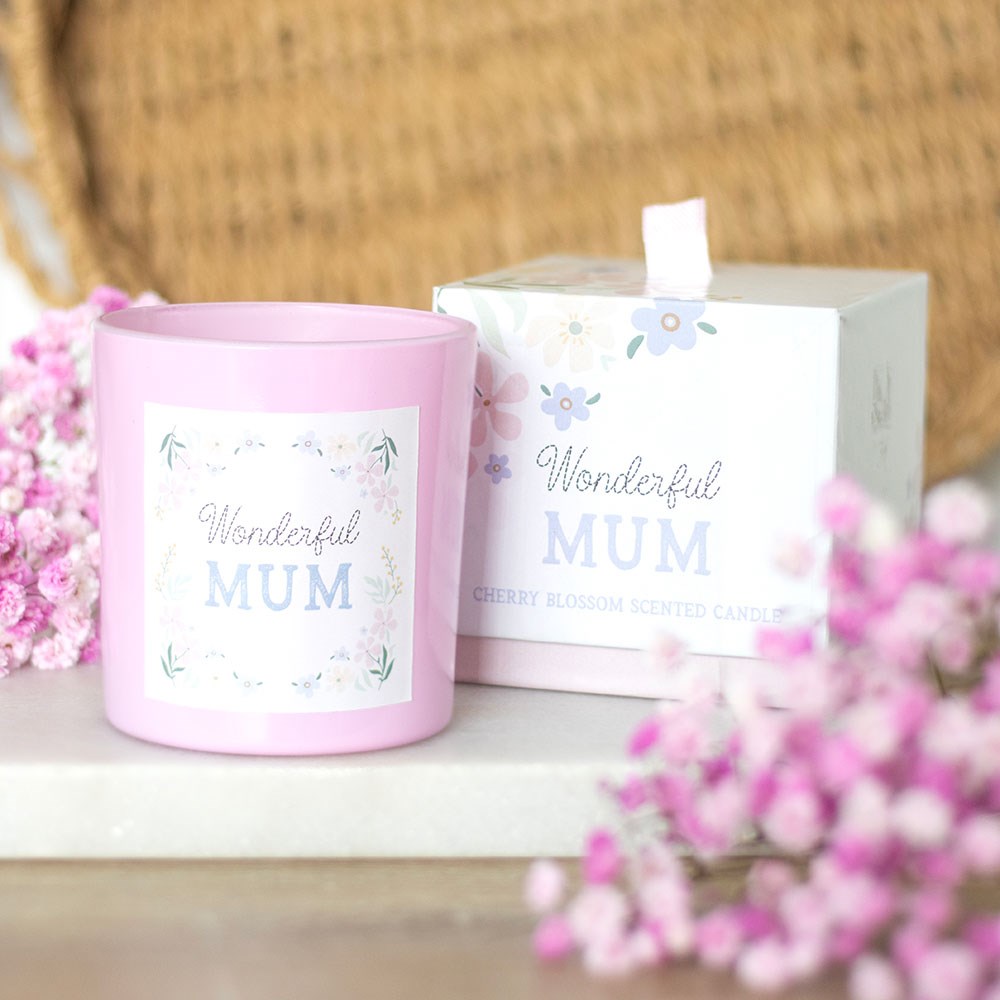 Pink candle with 'Wonderful MUM' text and floral design, surrounded by pink flowers on a wooden surface.