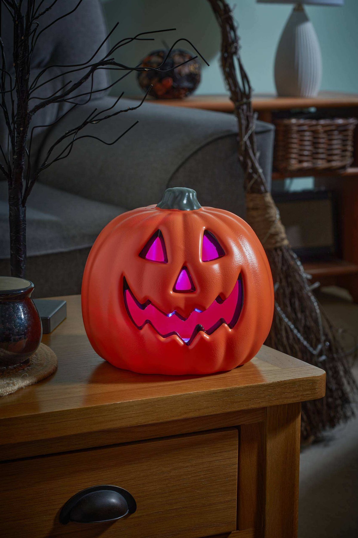 A glowing jack-o'-lantern Halloween decoration sitting on a wooden side table in a dimly lit living room.