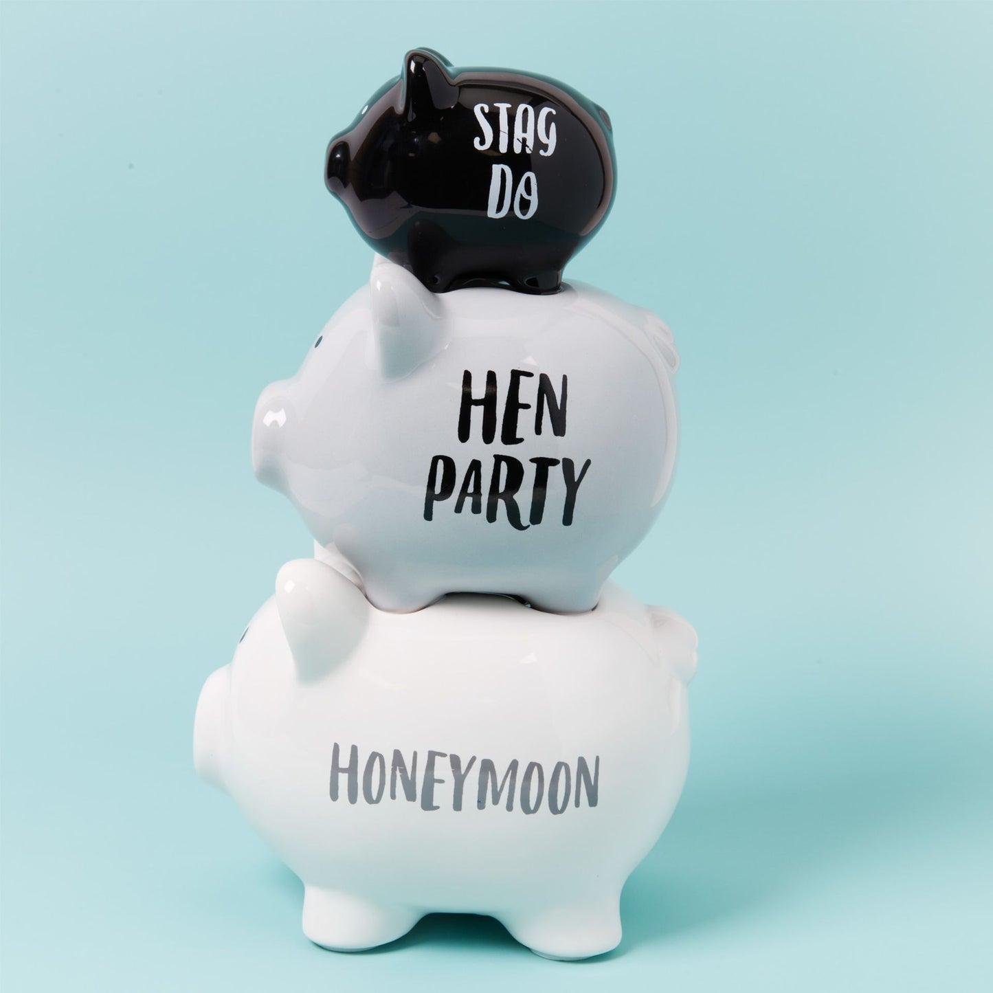 Stack of piggy banks with 'HEN PARTY', 'STAG DO', and 'HONEYMOON' text on a light blue background