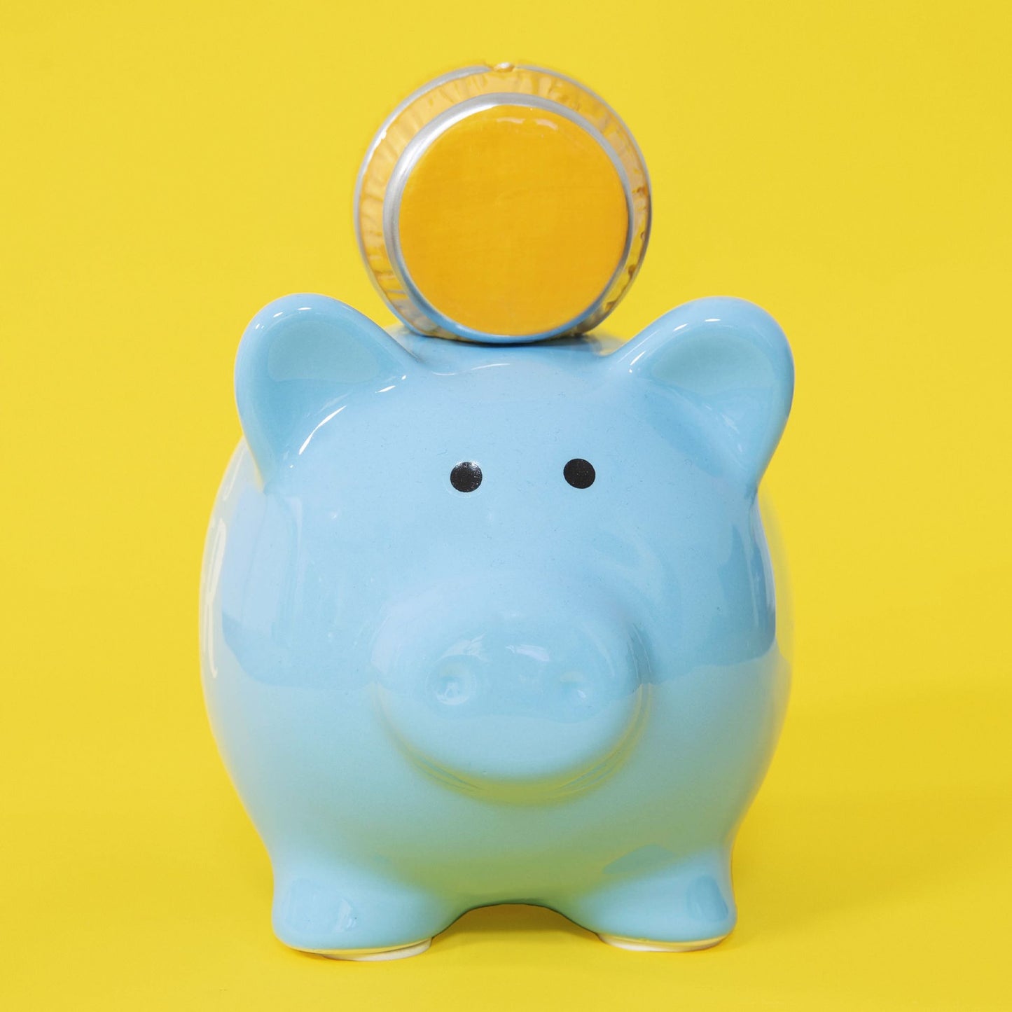 Blue piggy bank with a coin on a yellow background