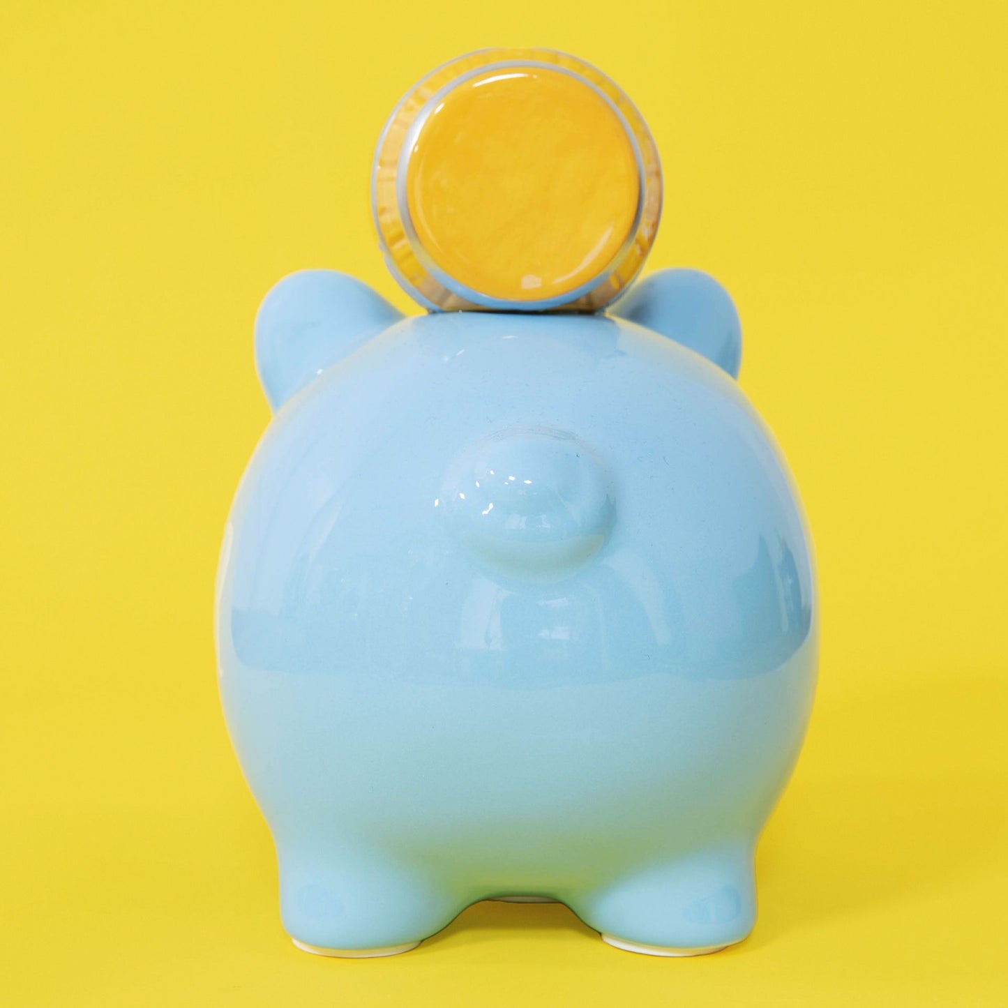 Blue piggy bank with a yellow coin on a yellow background