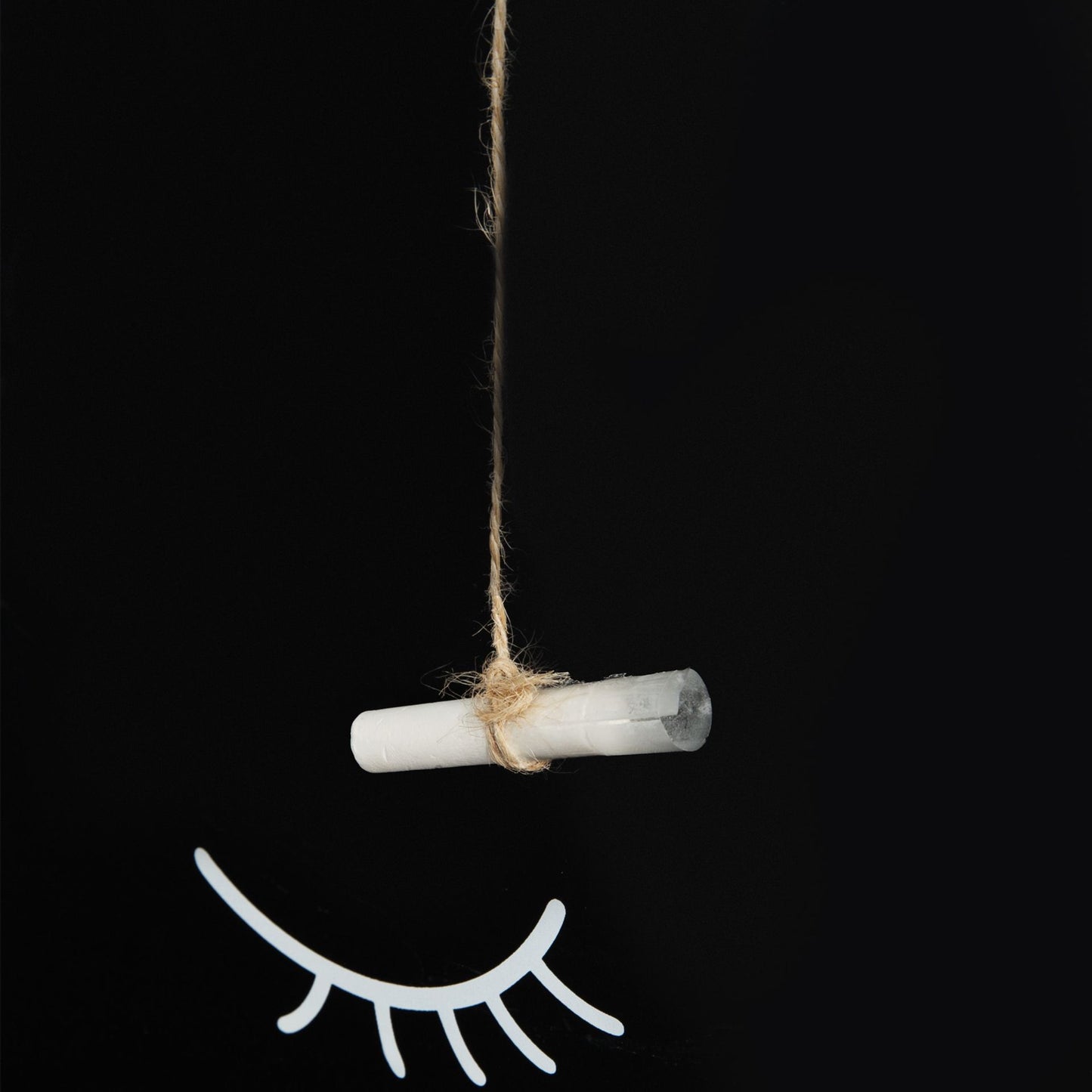 Crystal hanging from string with eyelash decoration on black background