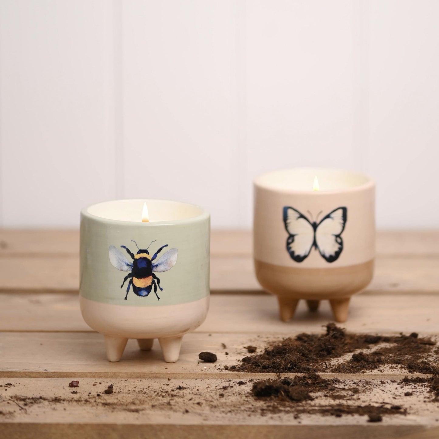 Two candles with bee and butterfly designs on a wooden surface.