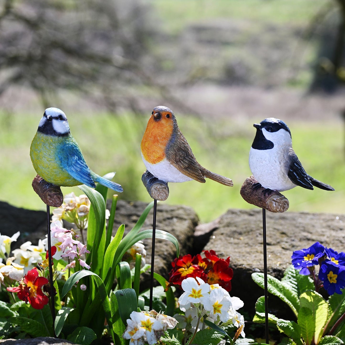 Three garden bird figurines on stakes with flowers in the background