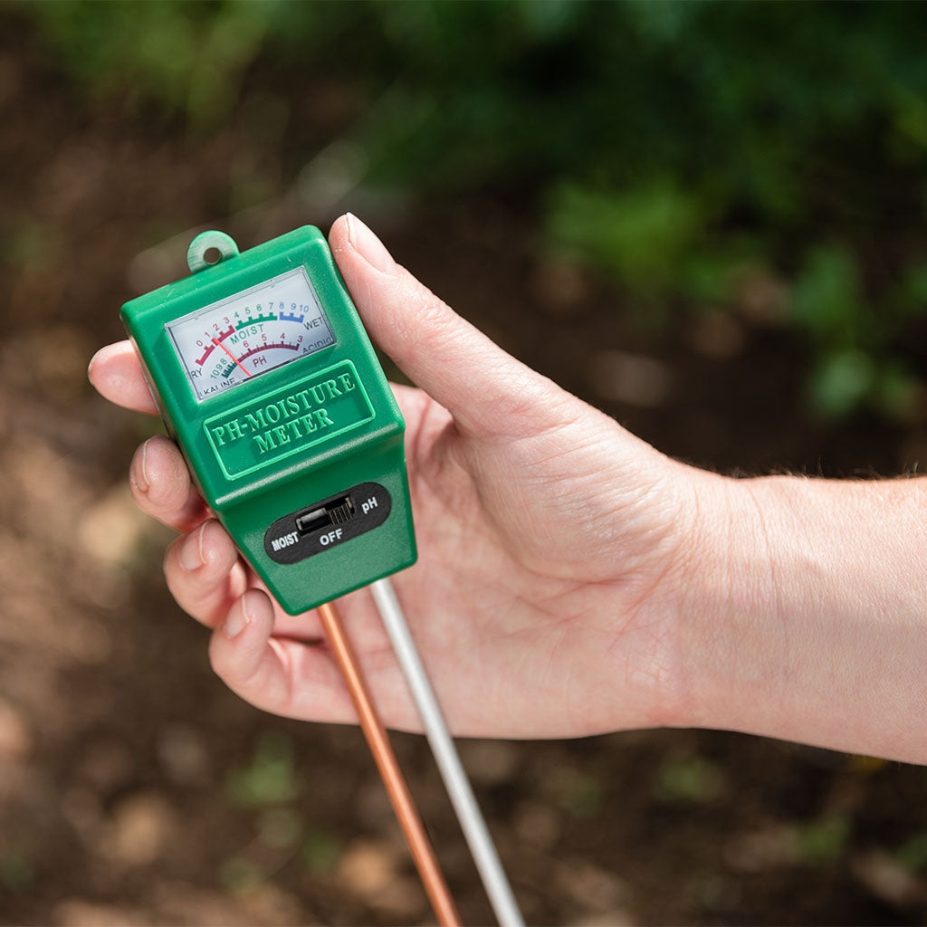 Hand holding a green soil moisture meter against a natural background