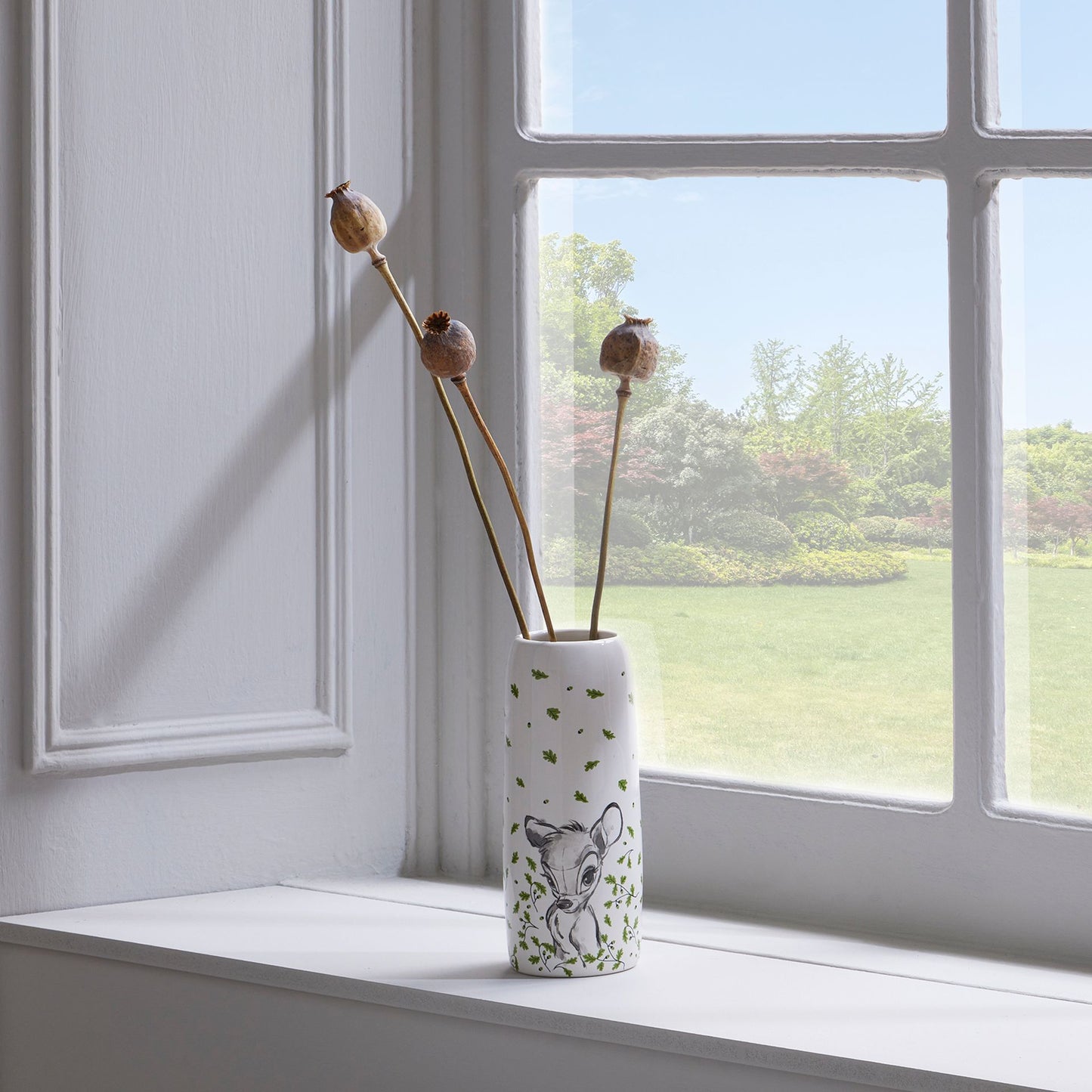 Vase with a deer design on a windowsill with dried plants, window in the background