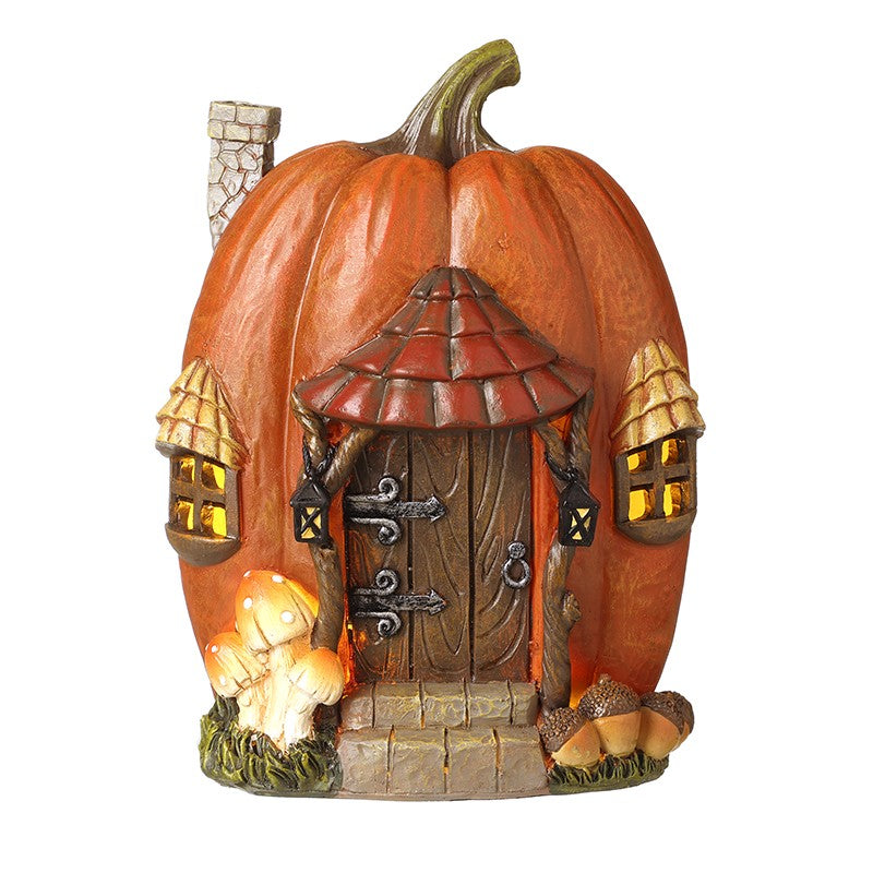 A decorative miniature pumpkin-shaped cottage with a carved wooden door, small roofed entryway, glowing windows, mushroom accents, and a small chimney, shown on a plain white background.