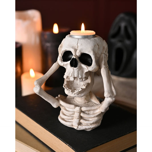 Skeleton candle holder with a lit candle on a dark surface