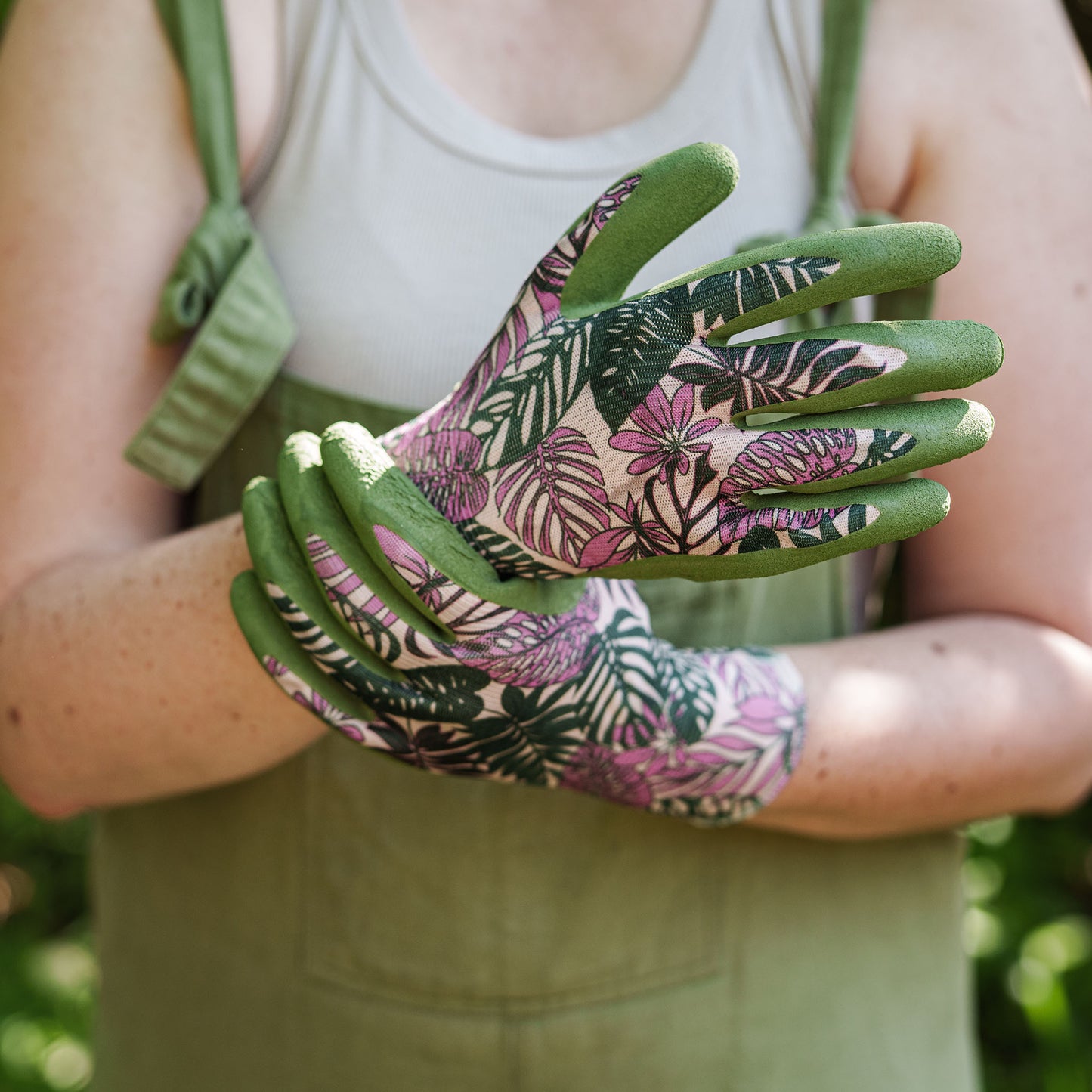 Person wearing floral gardening gloves with a green background
