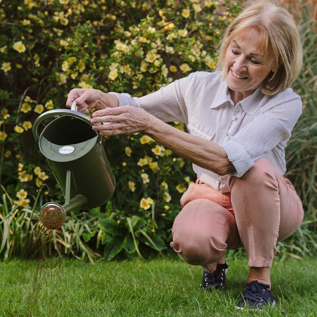 Woman gardening with a green watering can in a garden setting