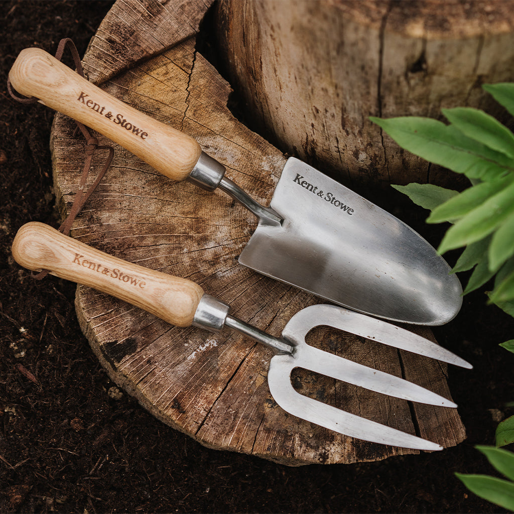 Gardening tools with wooden handles labeled 'Kent & Stowe' on a wooden surface.