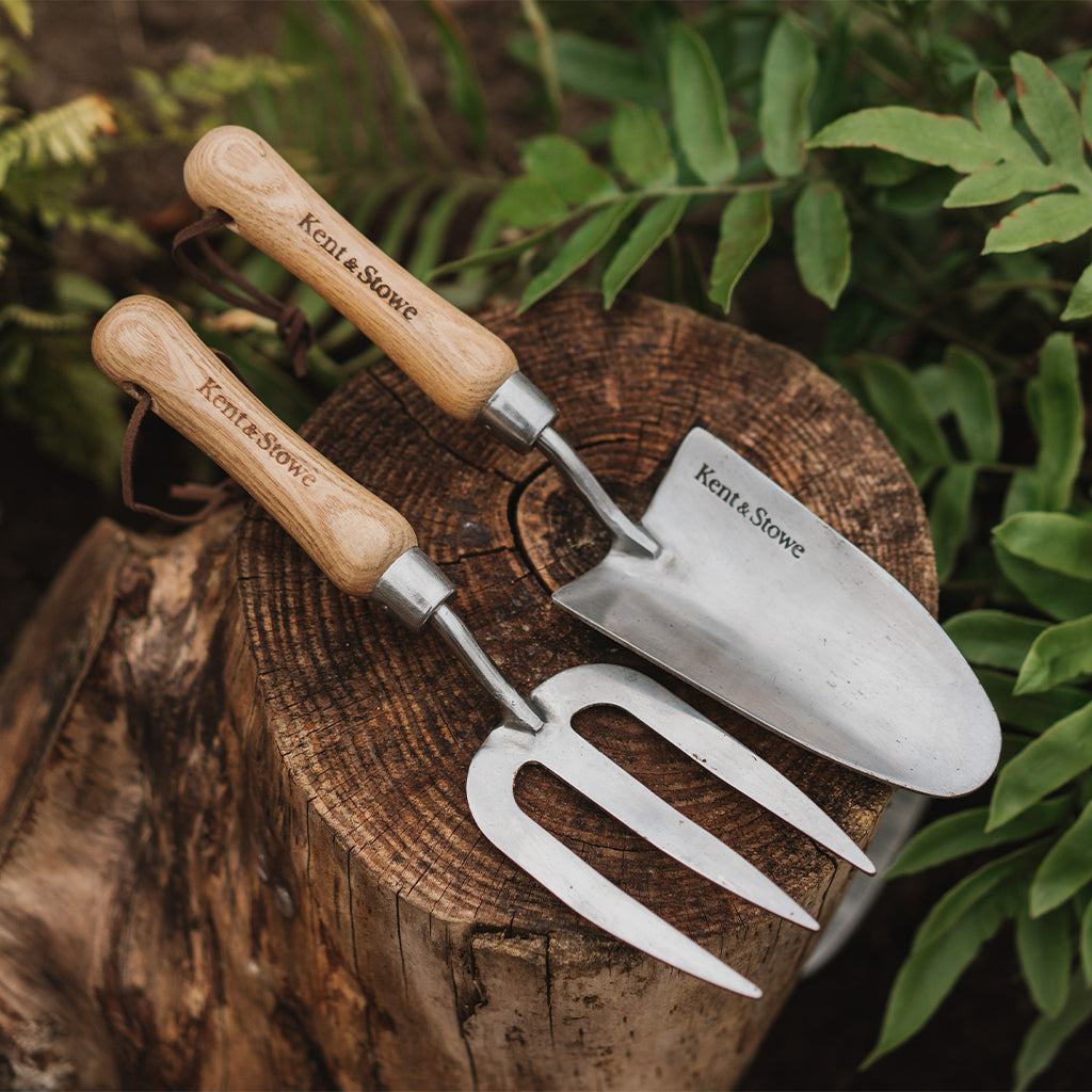 Gardening tools with wooden handles on a wooden stump surrounded by greenery