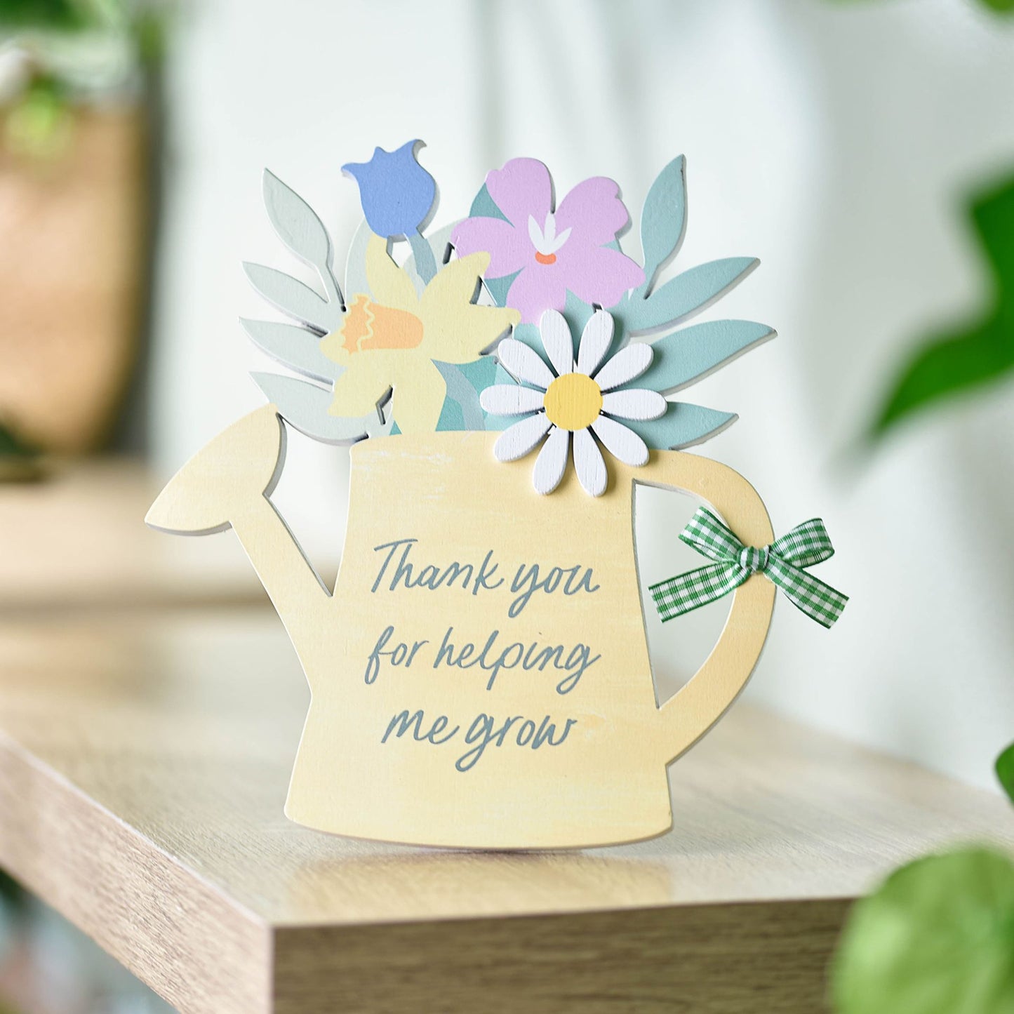 Decorative card shaped like a watering can with flowers and text on a wooden surface.