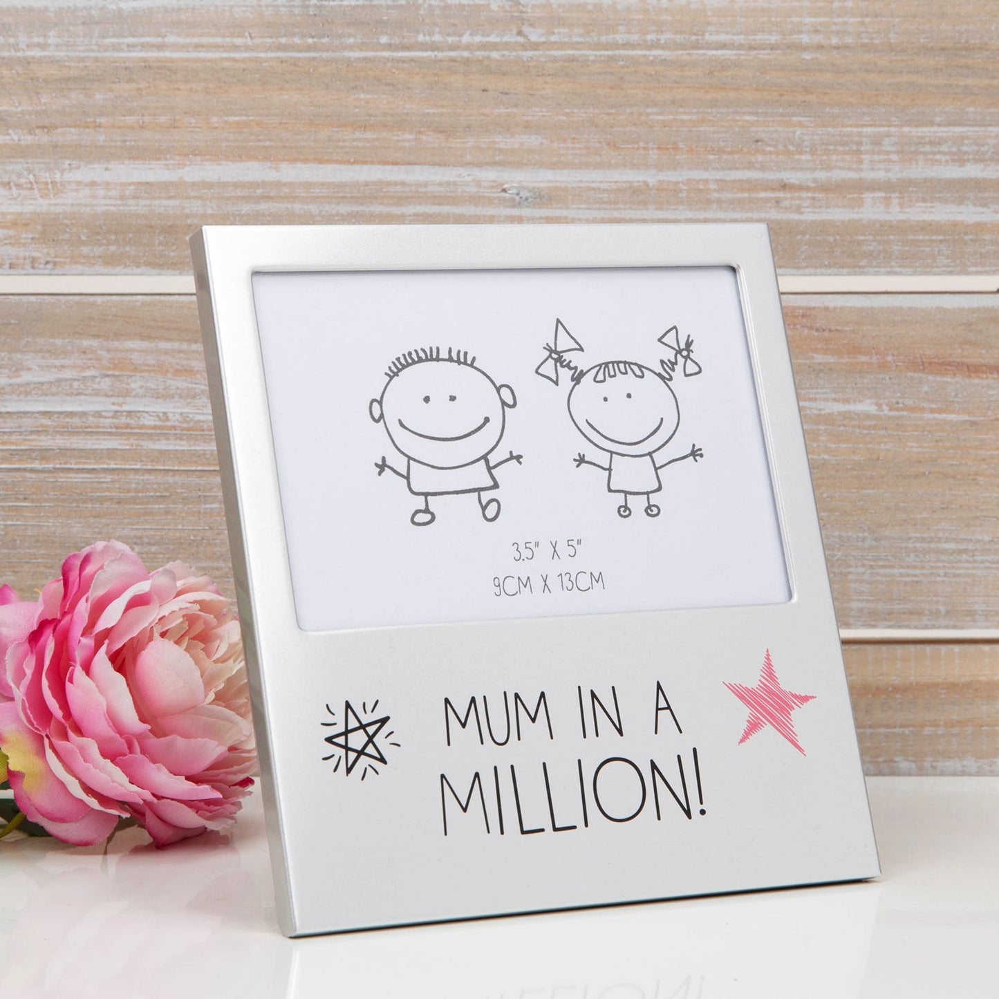 Framed artwork with 'Mum in a Million!' text and illustrations on a wooden surface with a pink flower.