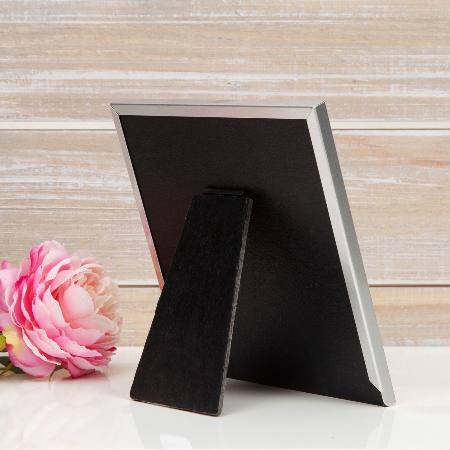 Black photo frame with a pink flower on a wooden surface