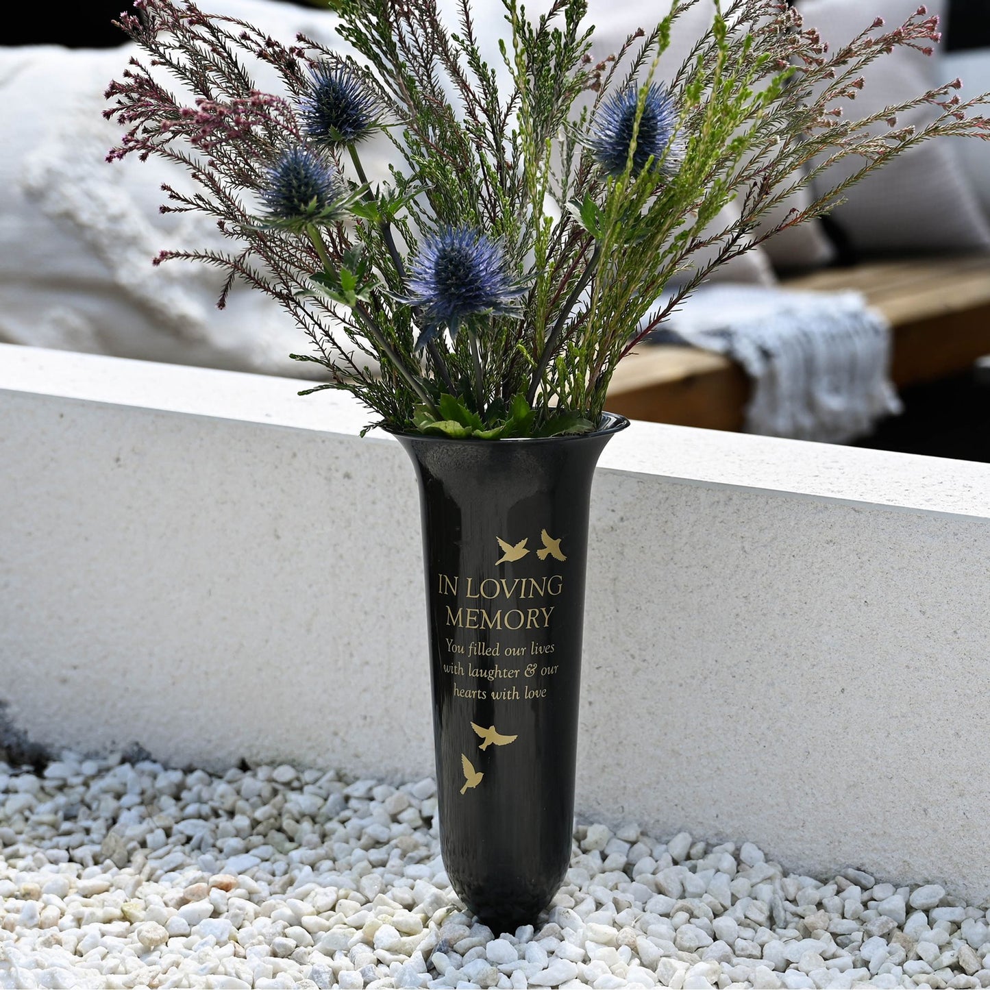 Vase with flowers labeled 'In Loving Memory' on a pebbled surface.
