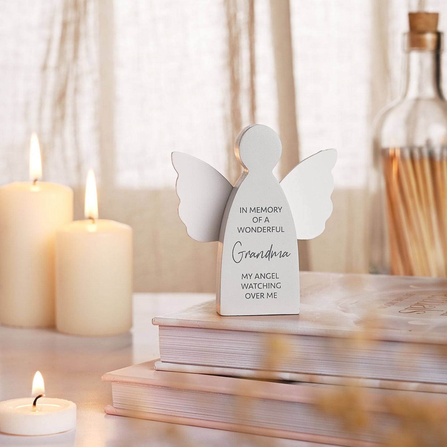 White angel figurine with engraved text on a table with candles and books.