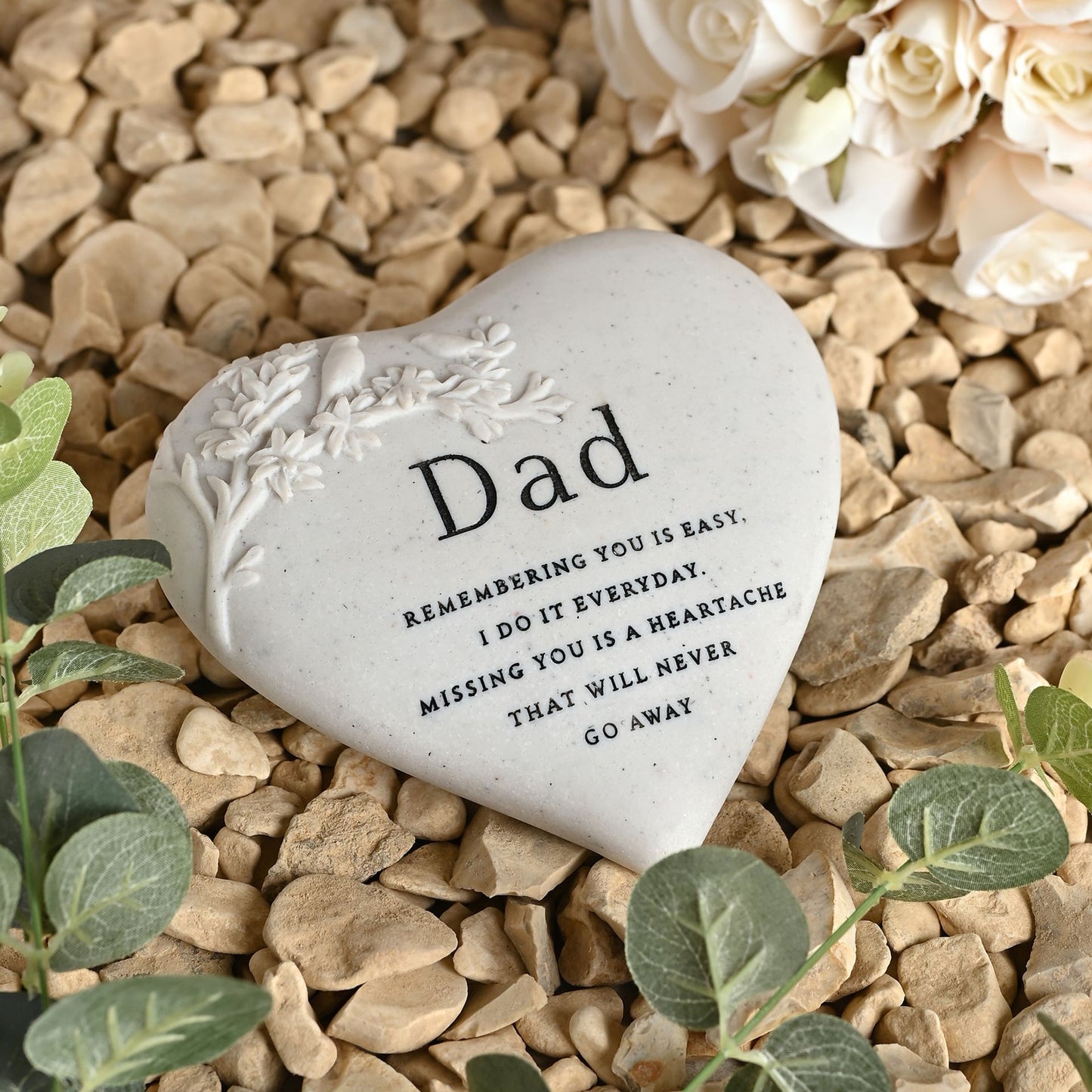 Heart-shaped stone with engraved message on pebbles and flowers