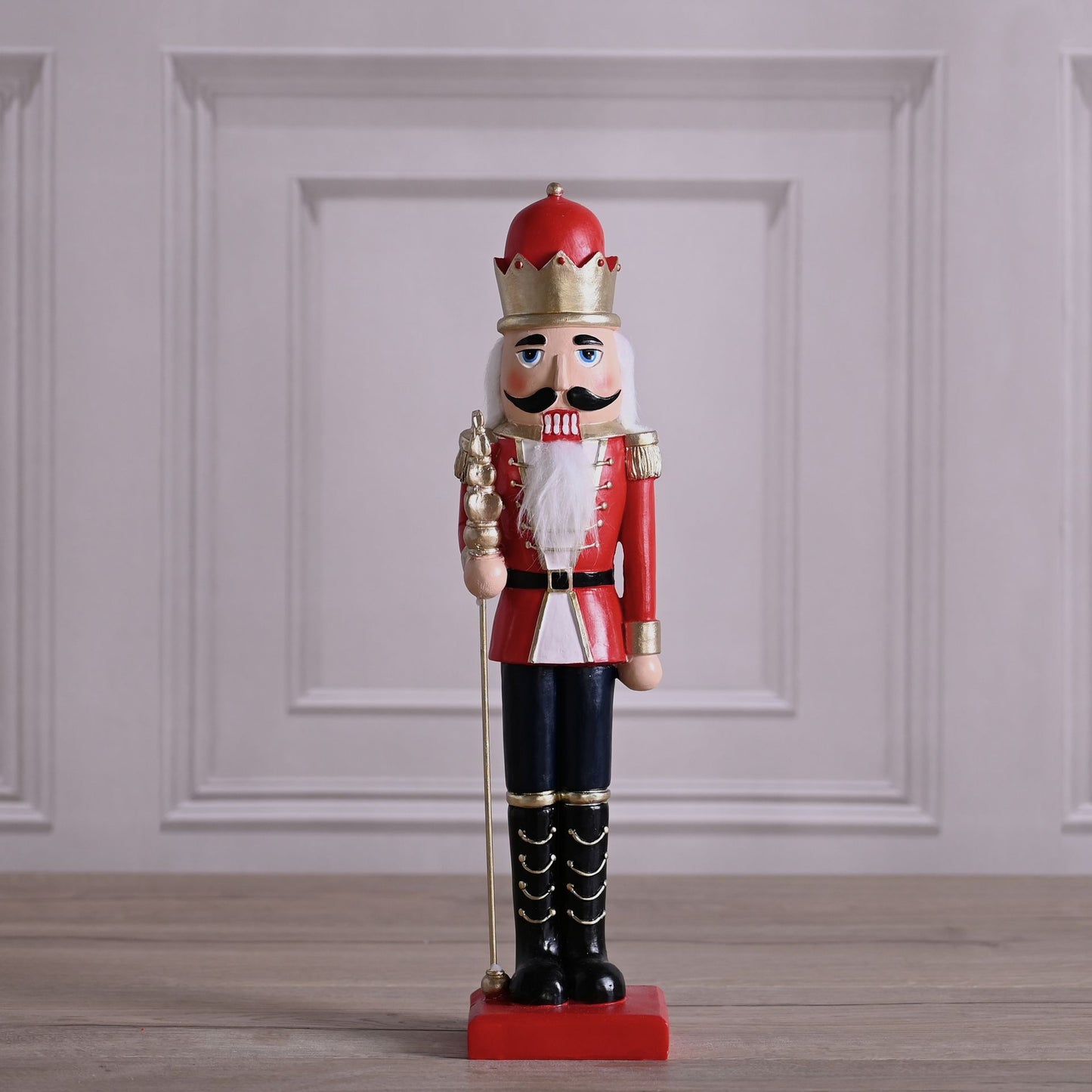 Decorative nutcracker figure with red outfit and crown on a wooden floor.