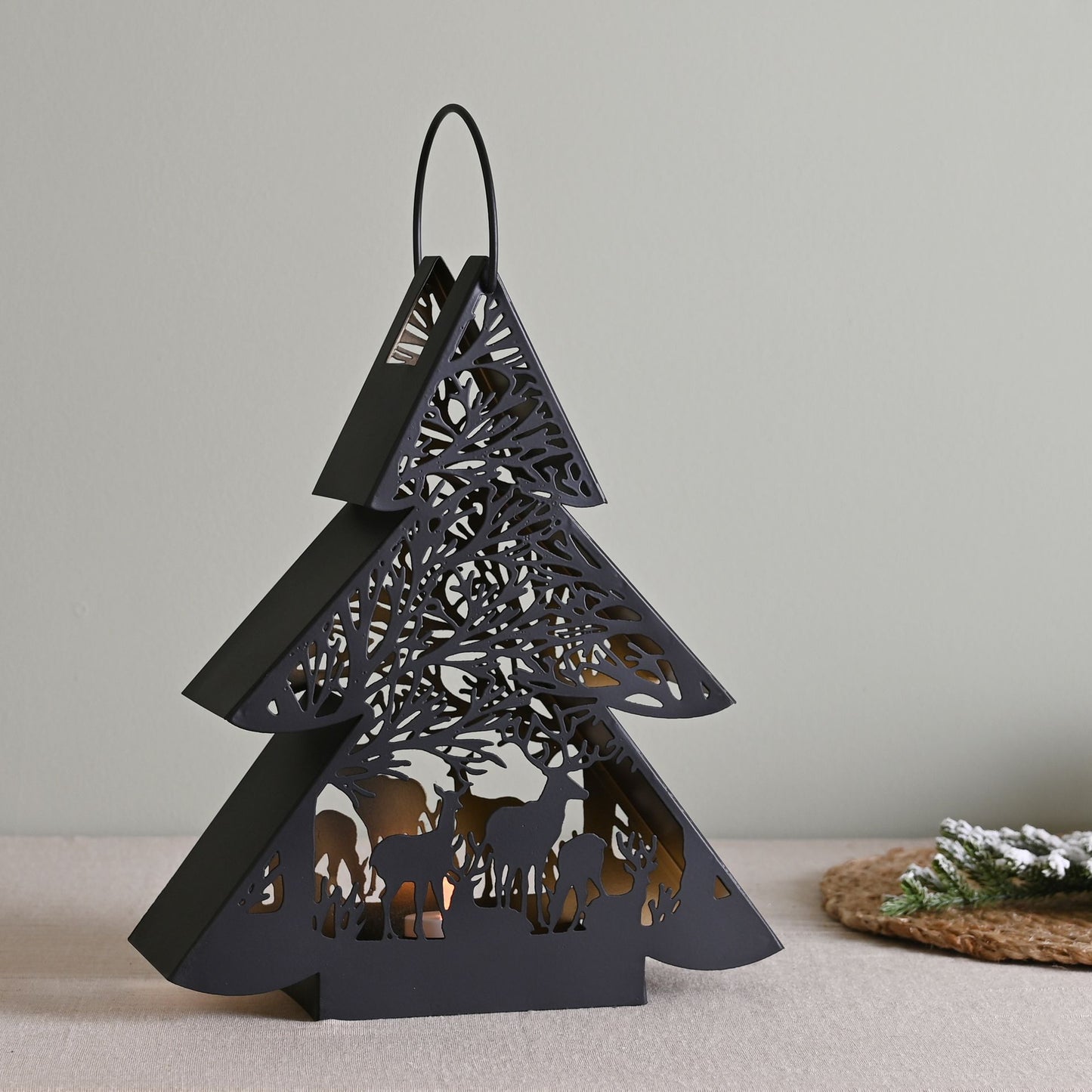 Black decorative lantern shaped like a Christmas tree with cut-out designs on a neutral background