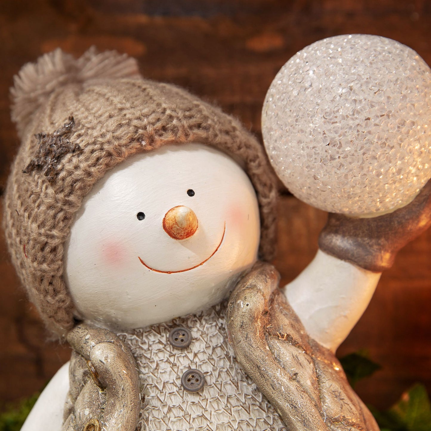 Decorative snowman figurine with a brown knitted hat and holding a light bulb against a blurred background.