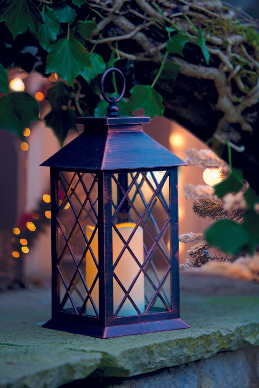 Decorative lantern with a warm glow on a stone surface with blurred lights and foliage in the background