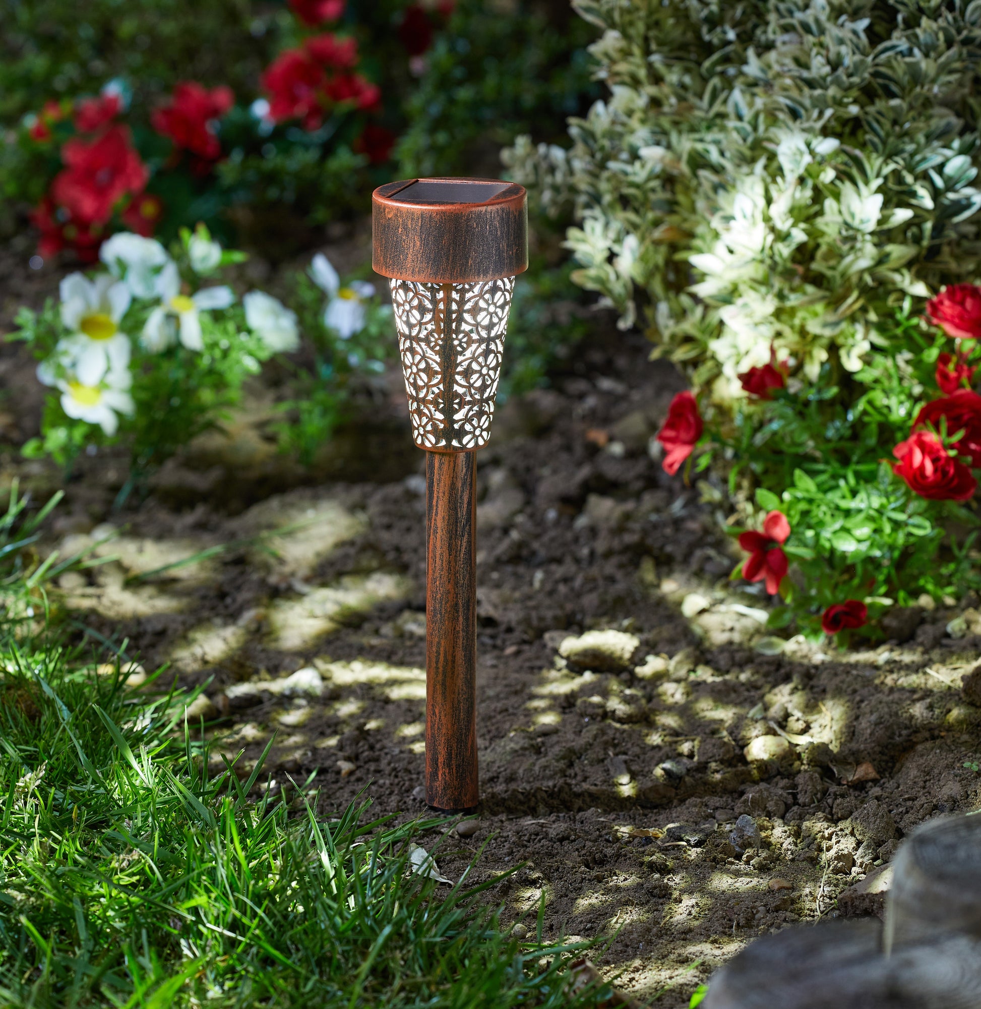 Decorative garden light in a garden setting with flowers and grass.
