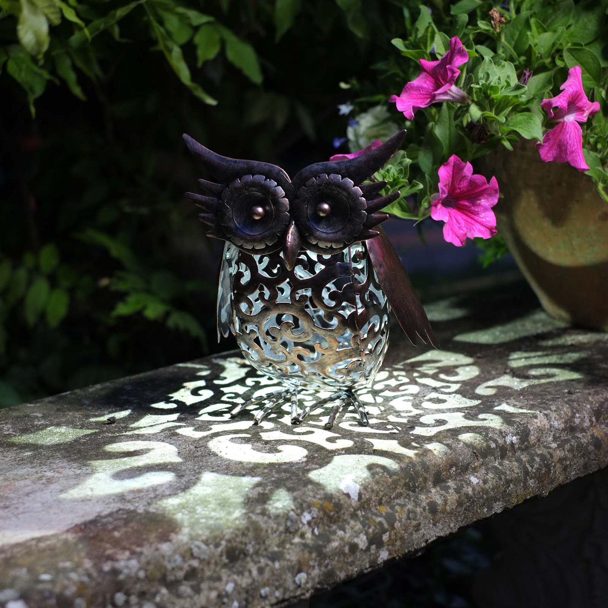 Decorative owl light casting a pattern on a stone surface with pink flowers in the background