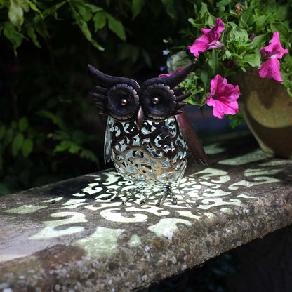 Decorative owl light casting a pattern on a stone surface with pink flowers in the background
