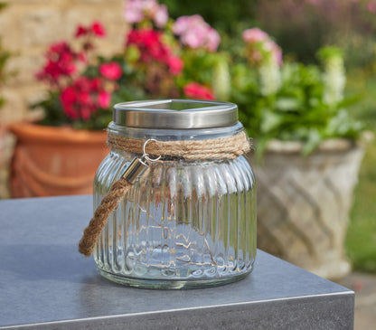 Glass lantern with solar light on a table outdoors with flowers in the background