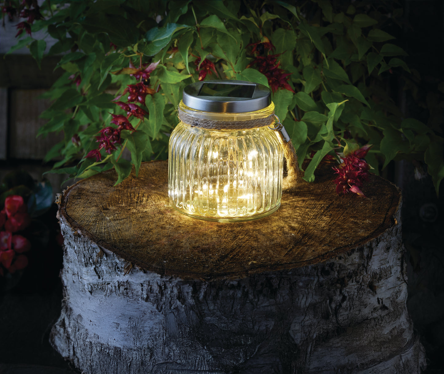 Solar lantern in a glass jar on a wooden stump with plants in the background