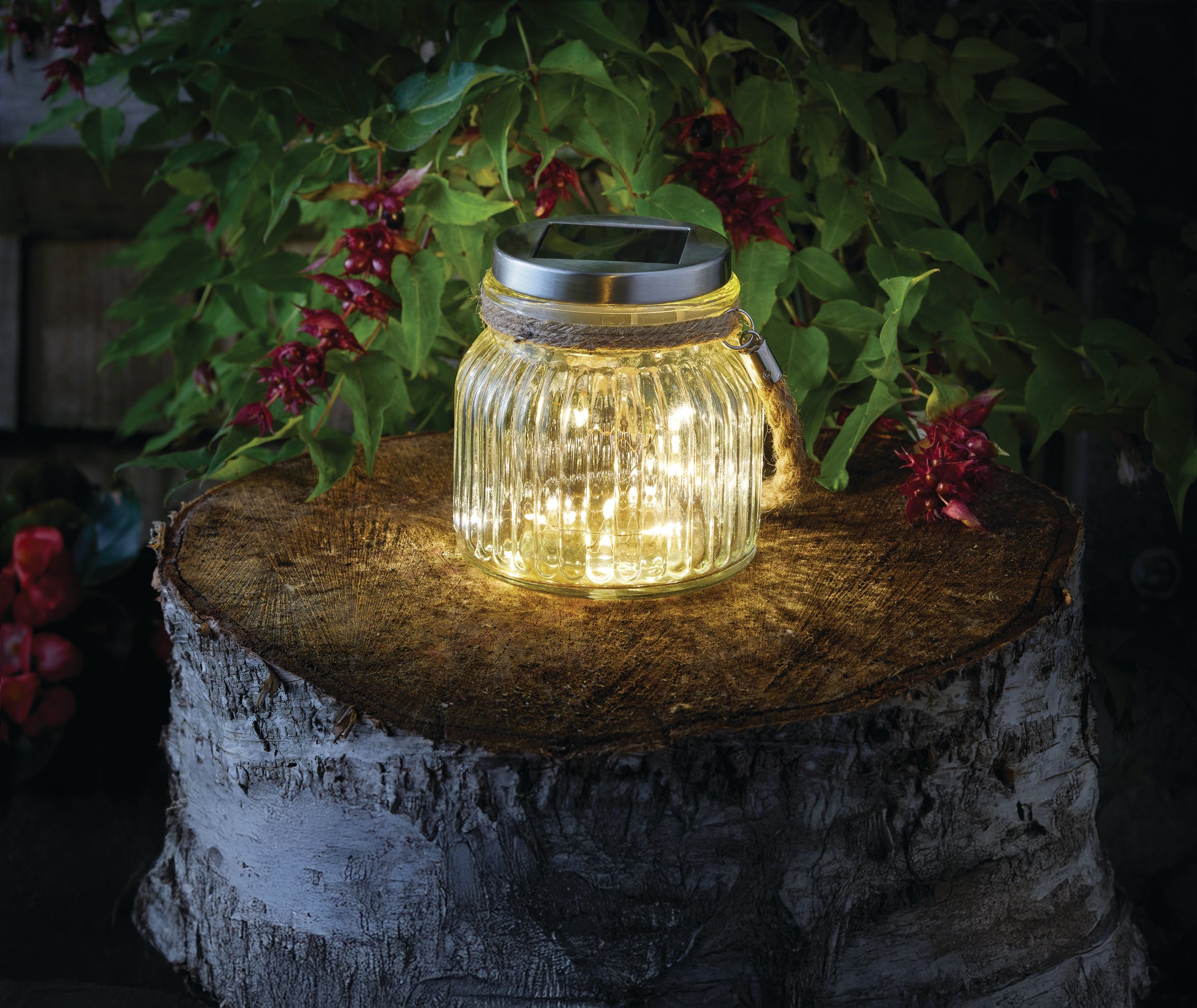 Solar lantern in a glass jar on a wooden stump with plants in the background
