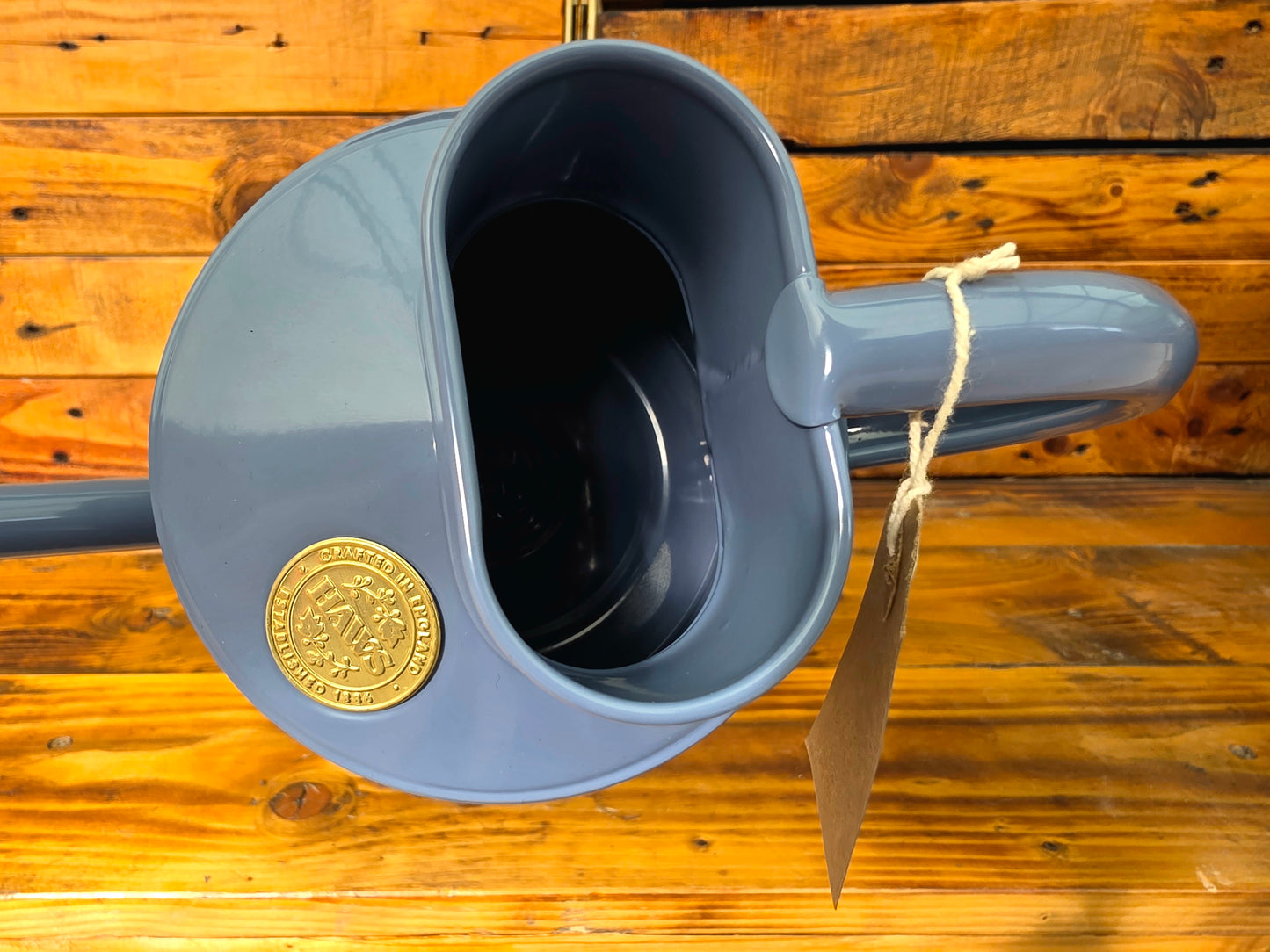 Blue watering can with a gold emblem on a wooden surface