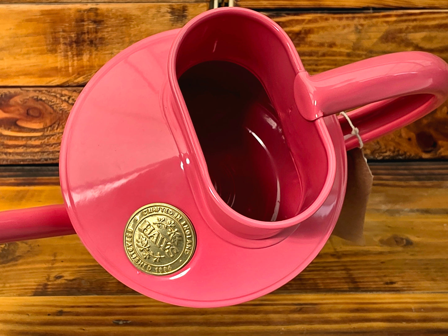 Pink watering can with a gold emblem on a wooden surface