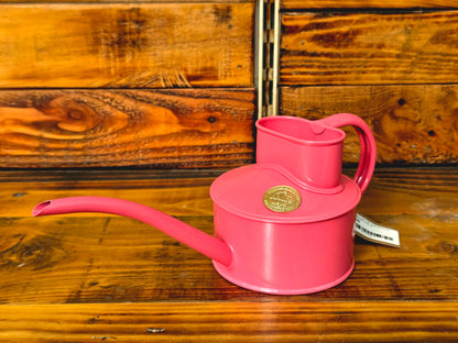 Pink watering can with a gold emblem on a wooden surface