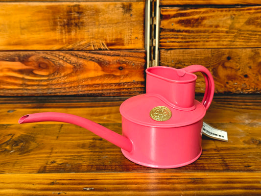 Pink watering can with a gold emblem on a wooden surface