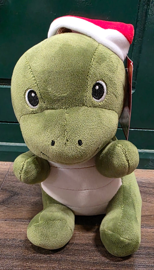 Green plush dinosaur toy wearing a red and white Santa hat on a wooden surface.
