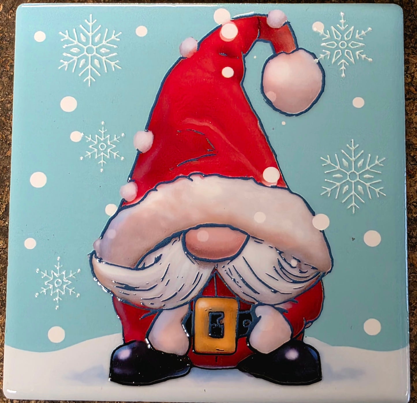 Decorative tile with a cartoon gnome wearing a red hat and outfit on a blue background with snowflakes.