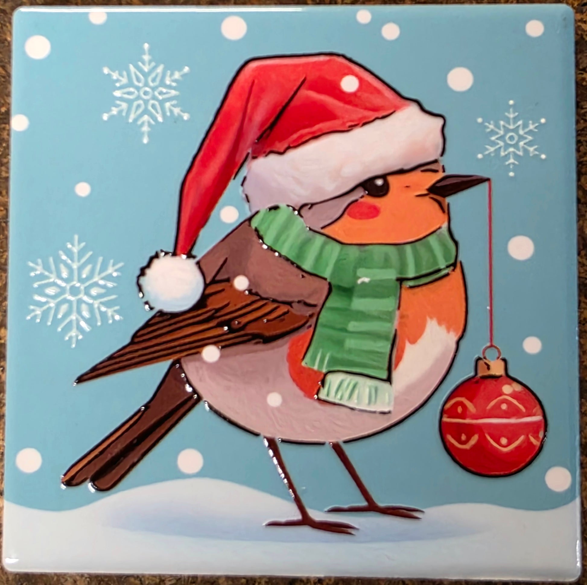 Illustration of a bird wearing a Santa hat and green scarf with snowflakes and a red ornament on a blue background.